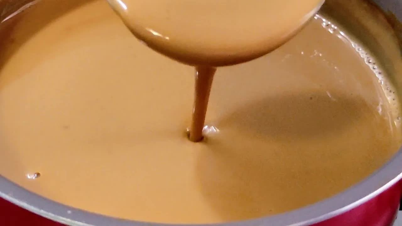 Leite queimado cremoso sendo mexido em panela vermelha