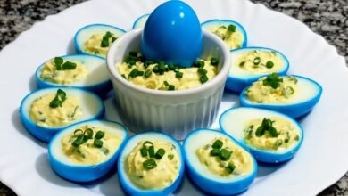 Ovos cozidos tingidos de azul, cortados ao meio e recheados com creme de gema e cebolinha, em prato branco ao redor de um potinho com recheio e um ovo azul inteiro