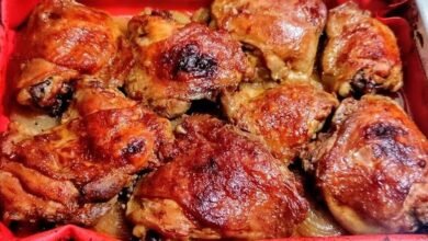 Sobrecoxas de frango assadas, douradas e suculentas, em assadeira forrada com tapete culinário vermelho sobre rodelas de cebola